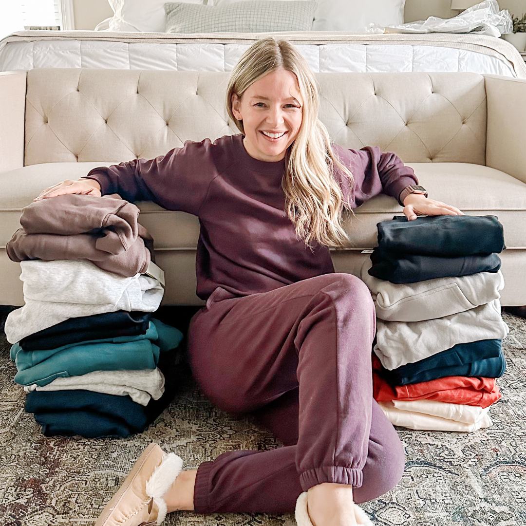 Brittney sitting with piles of sweatpants and sweatshirts on either side of her