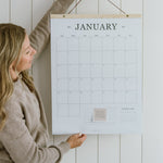 Woman hanging the 2027 family wall calendar, a large 18x24 hanging calendar on a cedar wood hanger