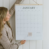 Woman hanging the 2027 family wall calendar, a large 18x24 hanging calendar on a cedar wood hanger