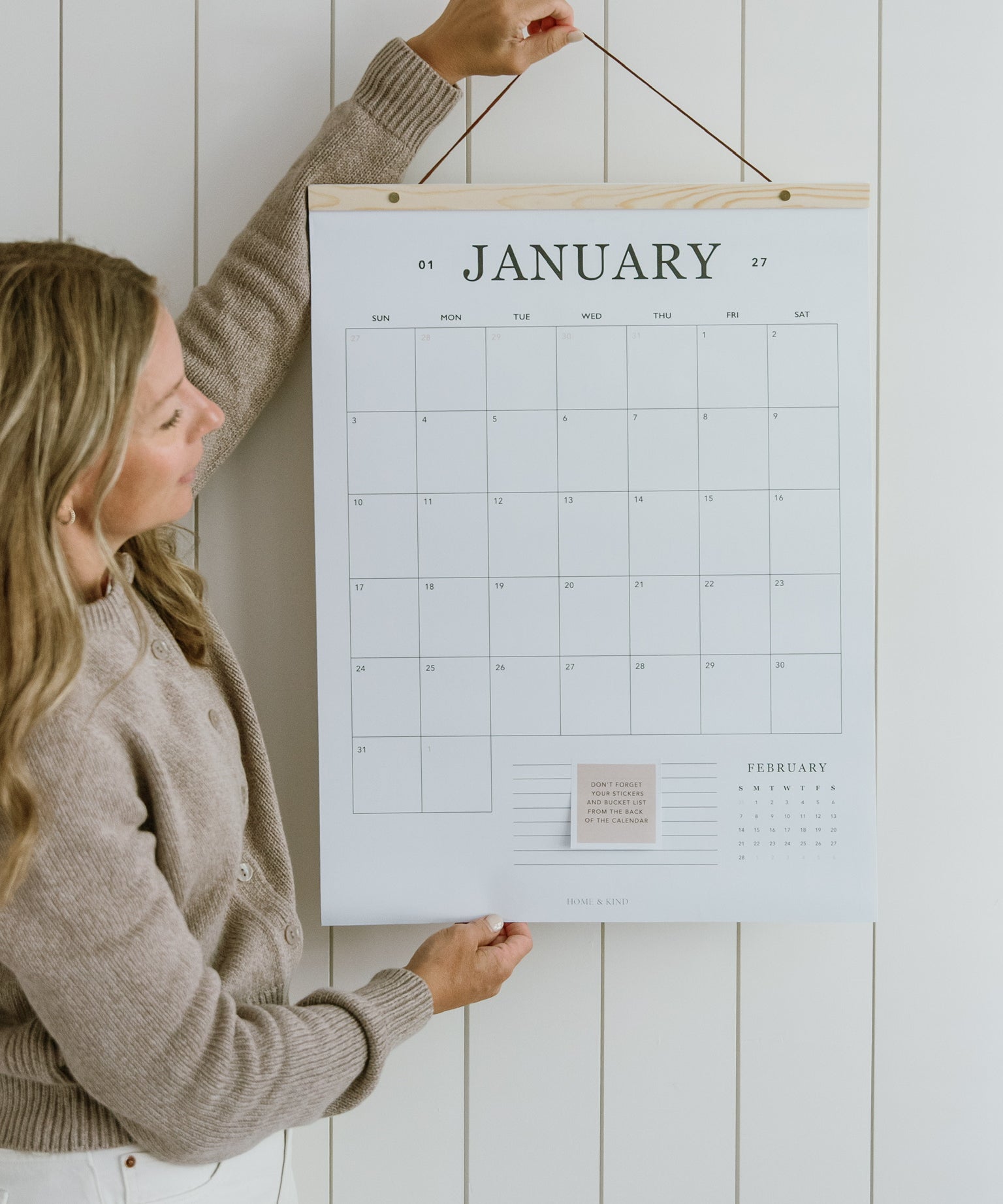 Woman hanging the 2027 family wall calendar, a large 18x24 hanging calendar on a cedar wood hanger