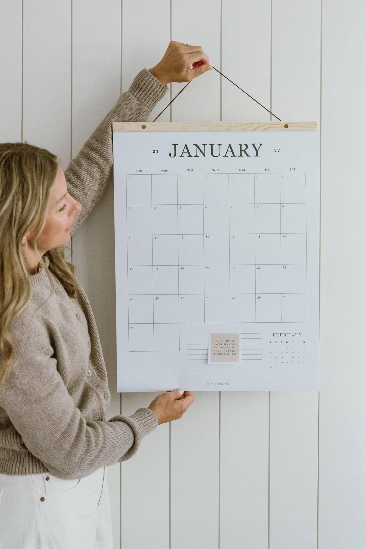 Woman hanging the 2027 family wall calendar, a large 18x24 hanging calendar on a cedar wood hanger