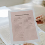 Hand holding a pink seasonal bucket list page from the family wall calendar