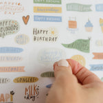 Hand peeling a happy birthday sticker from the family calendar sticker sheet