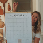 Woman holding up the 2027 family wall calendar and flipping through every page, from January to the 2028 preview.