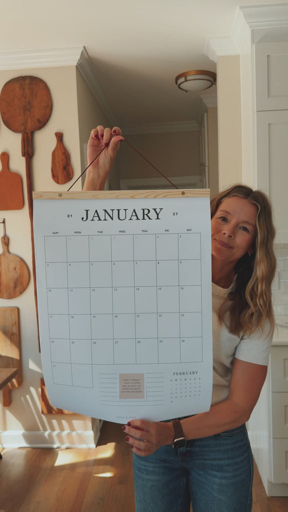 Woman holding up the 2027 family wall calendar and flipping through every page, from January to the 2028 preview.