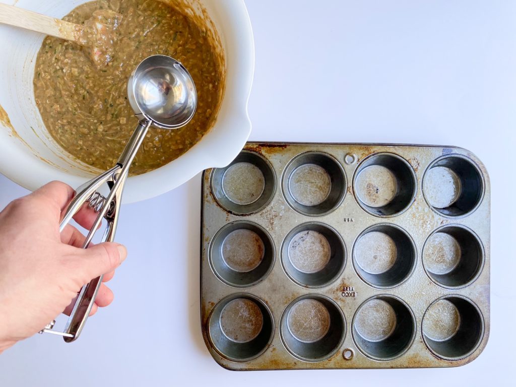 Zucchini muffin batter and a muffin tin on a table