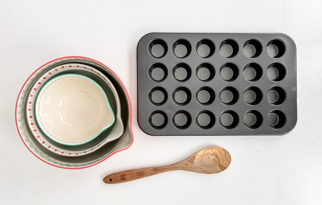A mixing bowl, mini muffin pan, and wooden spoon on a counter top